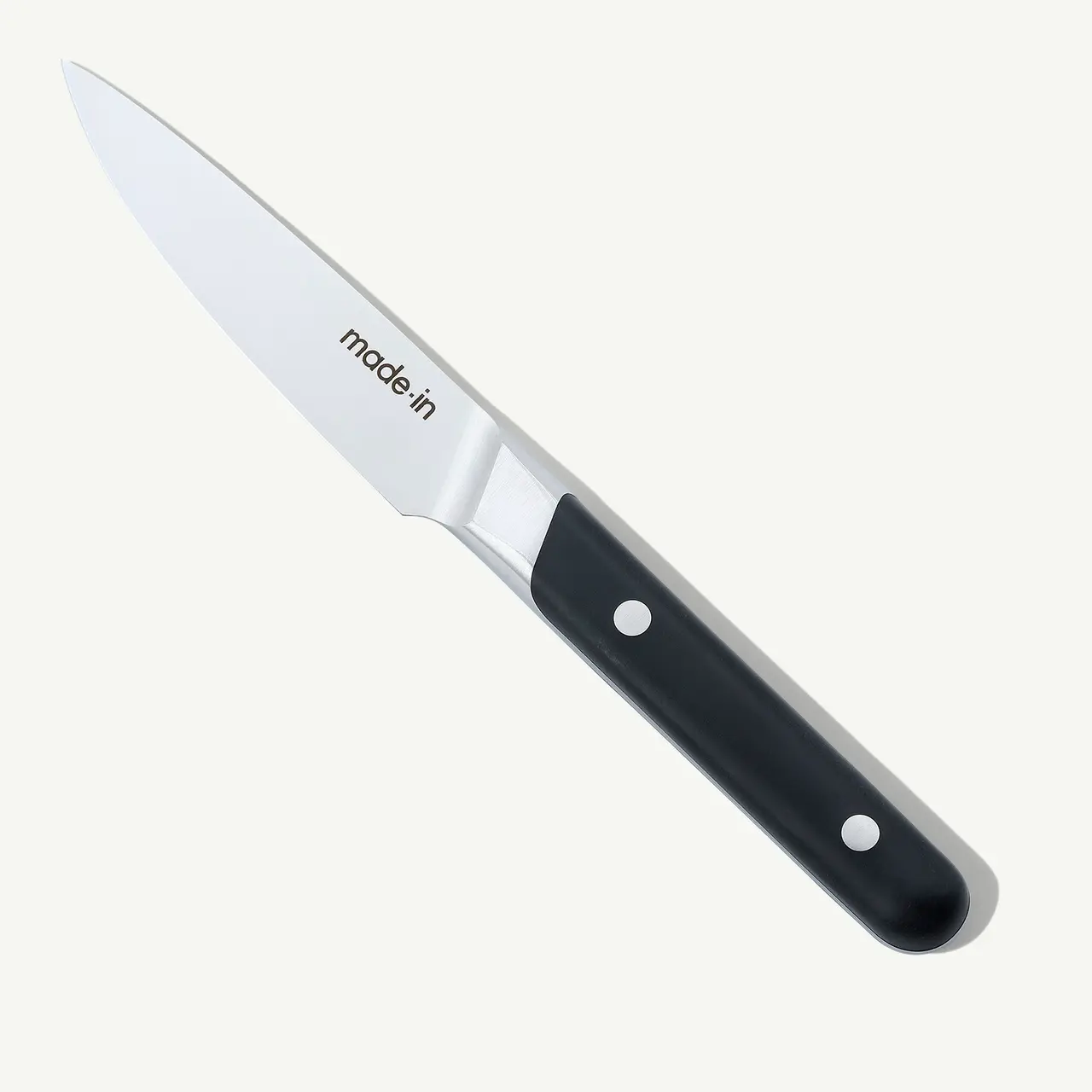 A stainless steel paring knife with a black handle is isolated against a white background.