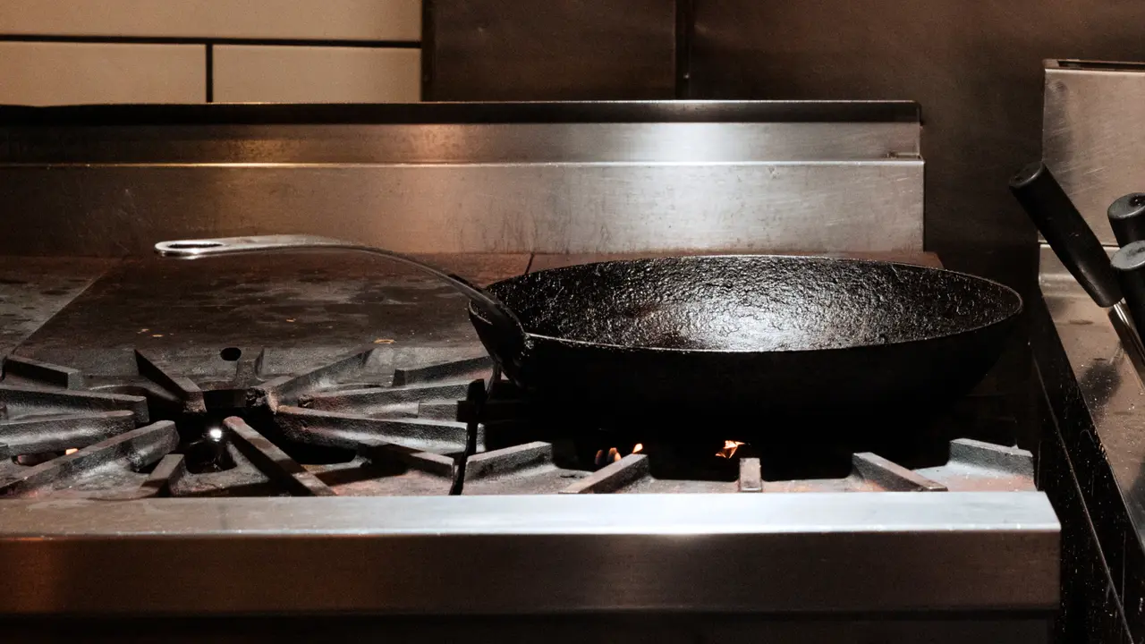 A seasoned cast iron skillet sits on a gas stove top with an industrial kitchen setting in the background.