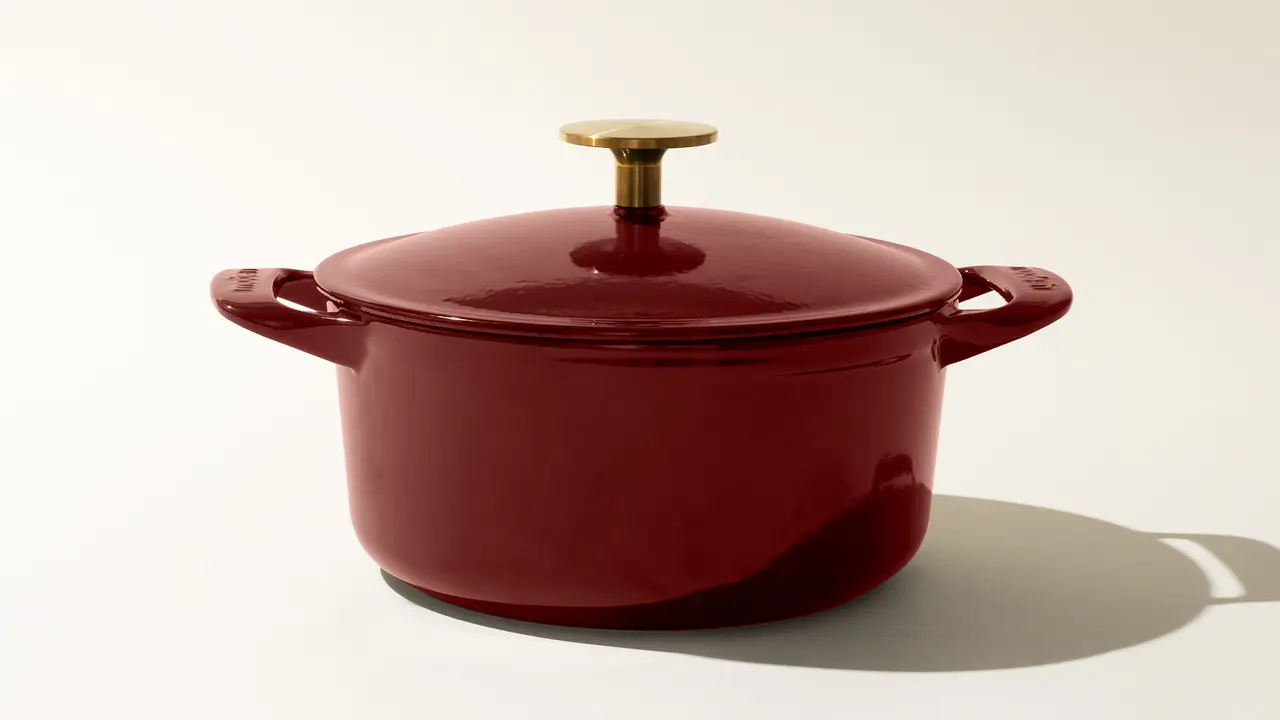 A red enameled cast iron Dutch oven with a lid and a gold-colored knob on a light background.
