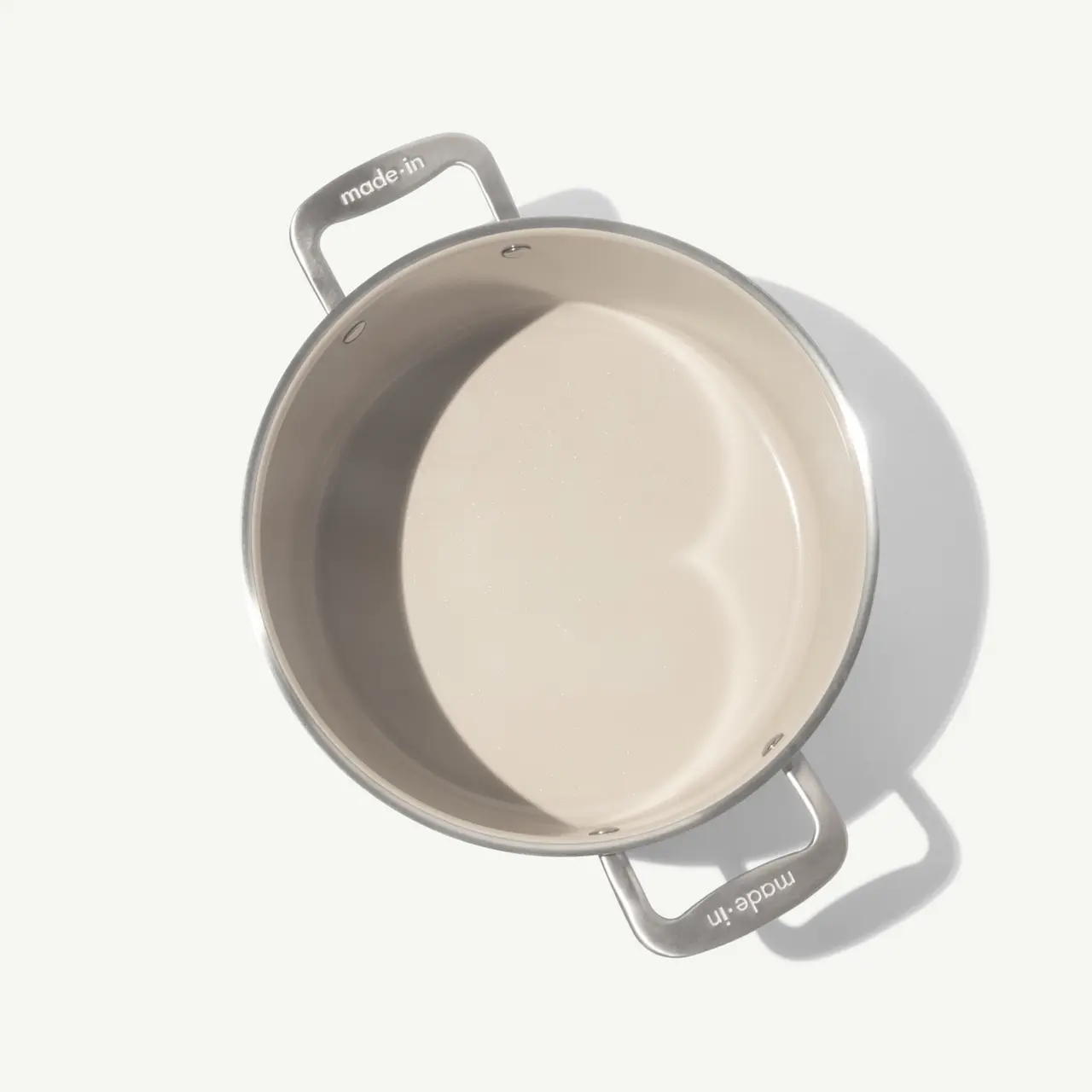 A stainless steel pot with two handles sits against a light background, showcasing its smooth interior.