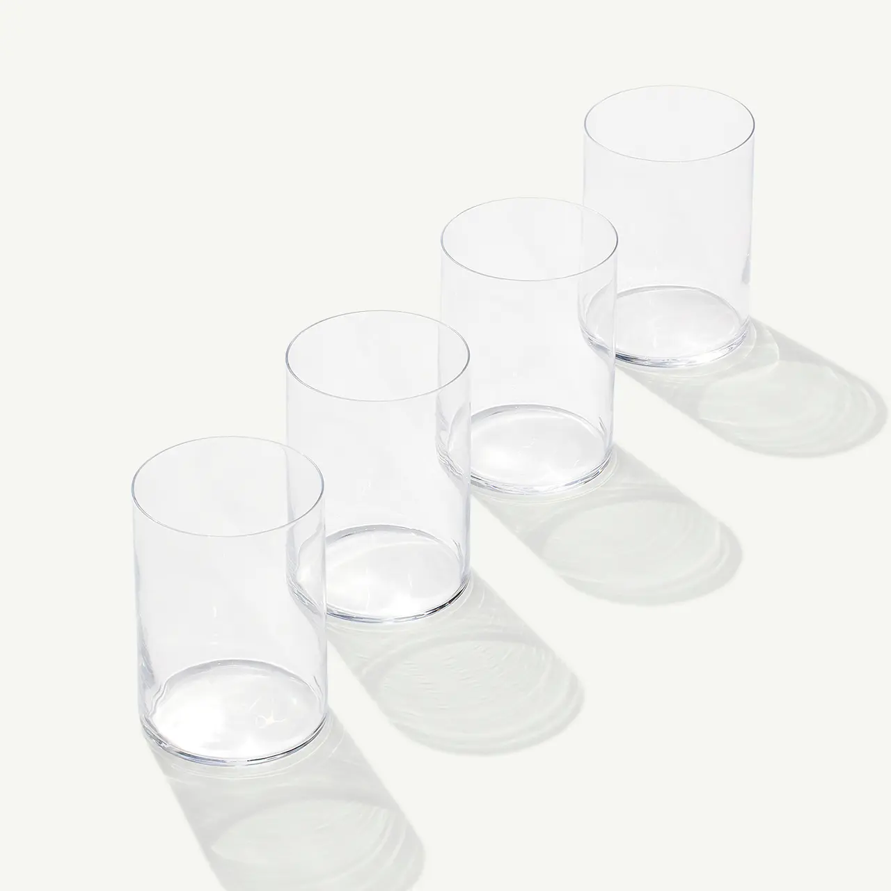Four empty clear glasses are arranged diagonally casting soft shadows on a light surface.
