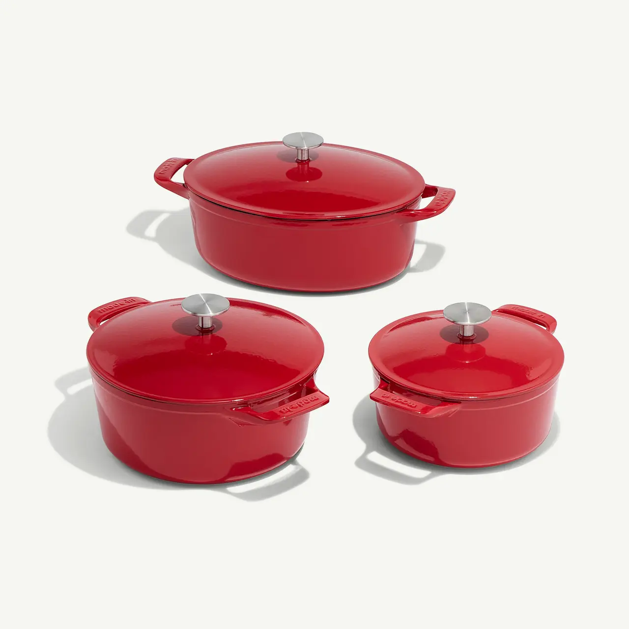 Three red Dutch ovens with silver knobs on the lids are arranged on a light background.