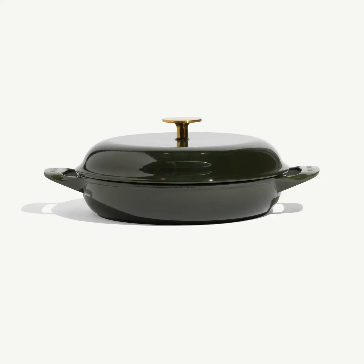 A green, round enameled cast iron cooking pot with a gold knob on the lid, resting on a light background.
