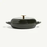 A green, round enameled cast iron cooking pot with a gold knob on the lid, resting on a light background.