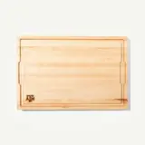 A rectangular wooden cutting board with a smooth surface and a logo in the bottom corner.