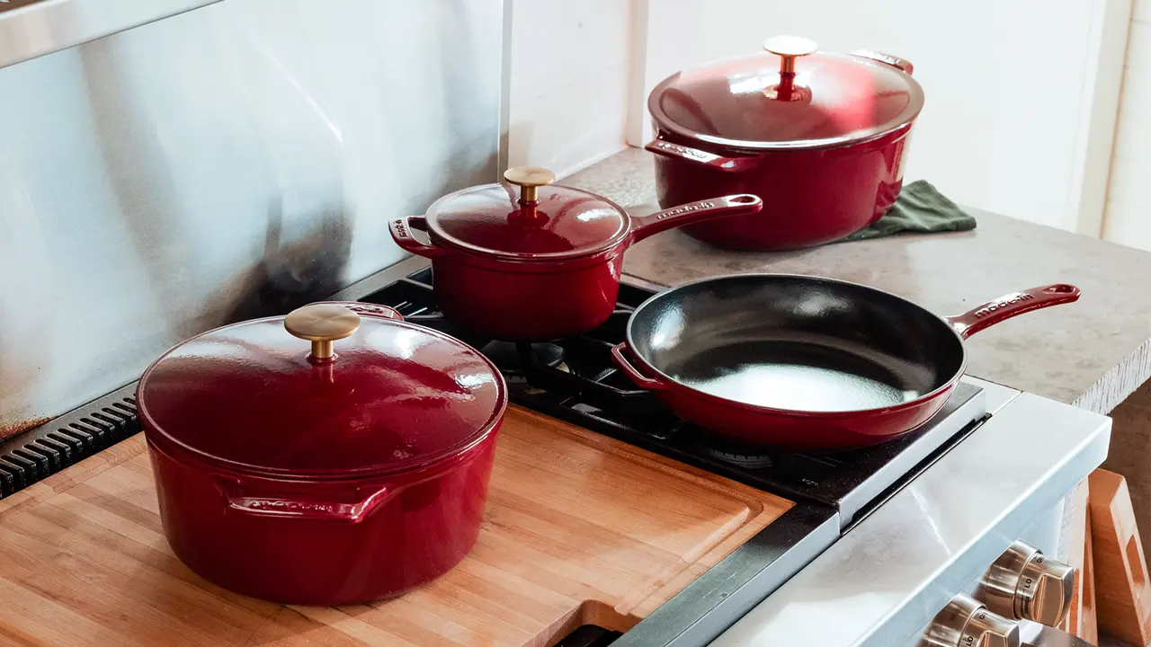 A set of red cookware, including pots and a frying pan, is placed on a stovetop in a kitchen.