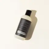 A bottle with a label and barcode lies against a plain background, casting a soft shadow.