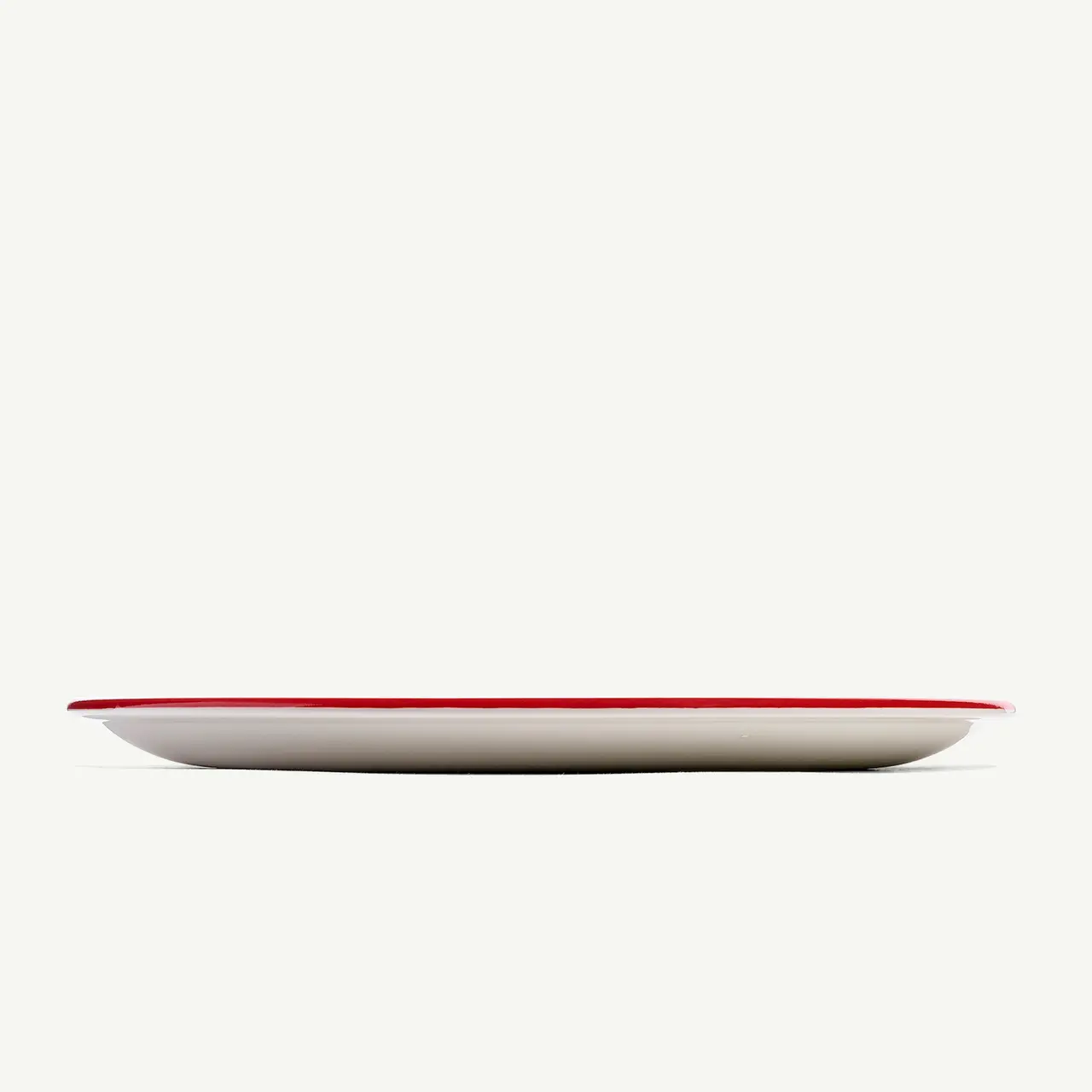 A side view of a plain white plate with a red rim on a pale background.