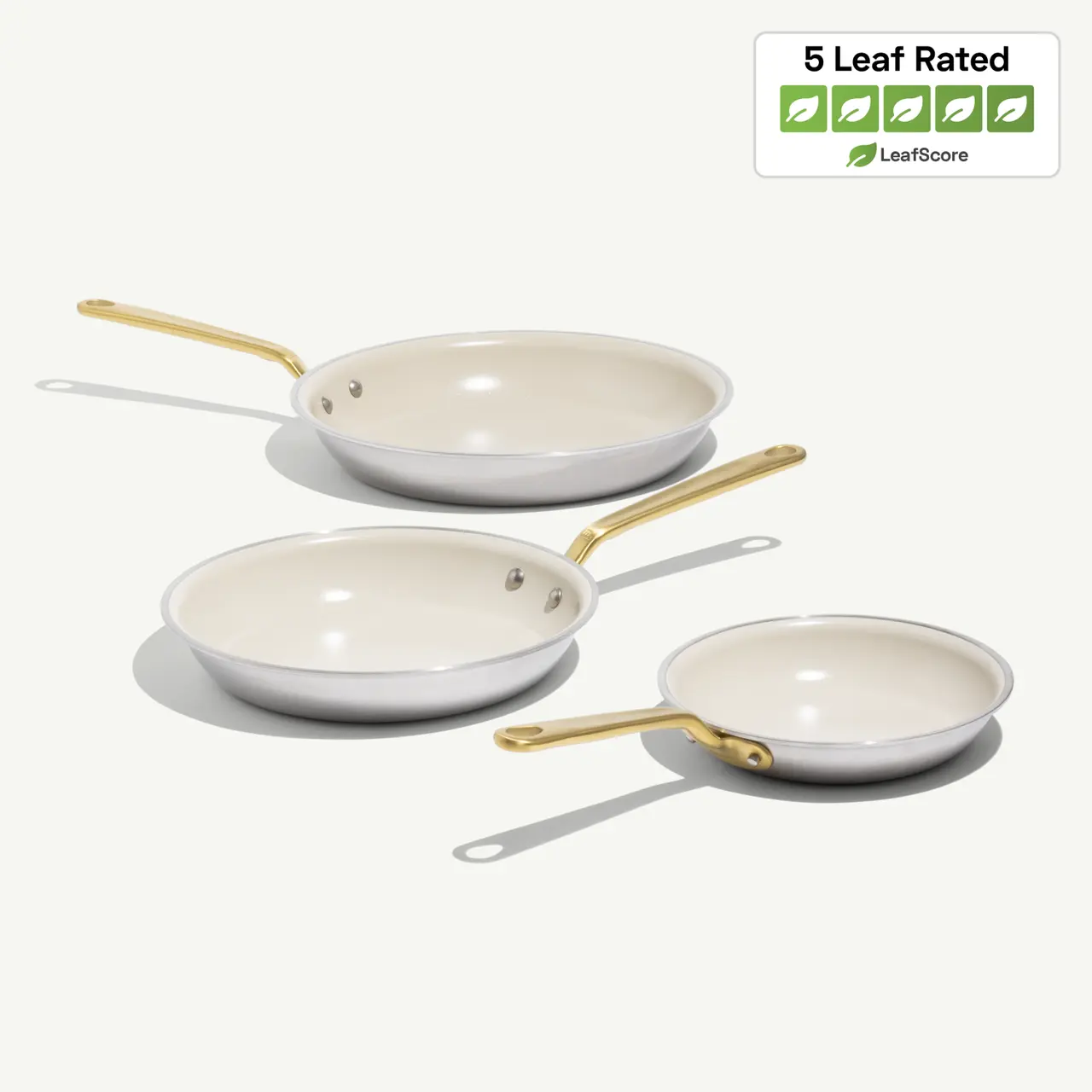 Three frying pans of varying sizes with a gold handle and a light-colored non-stick interior, accompanied by a "5 Leaf Rated" eco-friendly label.