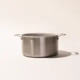 A stainless steel cooking pot with two handles is centered on a plain background, casting a soft shadow to the side.