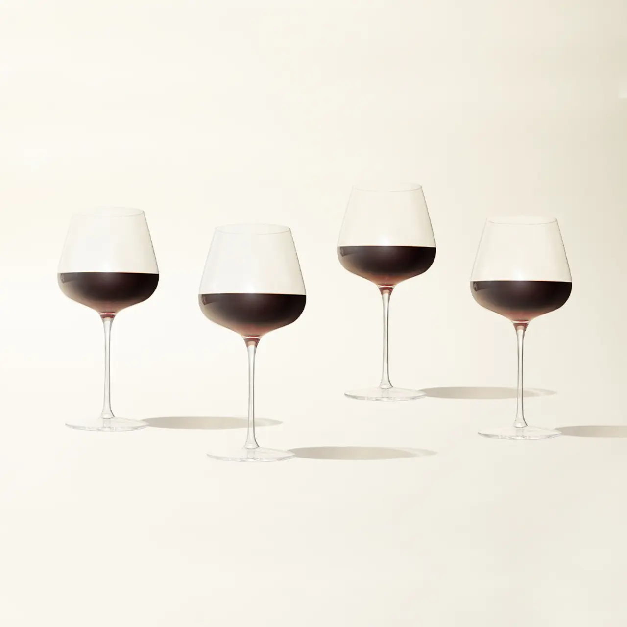 Four wine glasses with varying levels of red wine against a light background.