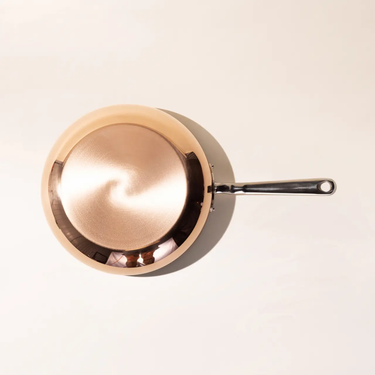 A copper-colored frying pan with a black handle is positioned on a light surface, viewed from above.