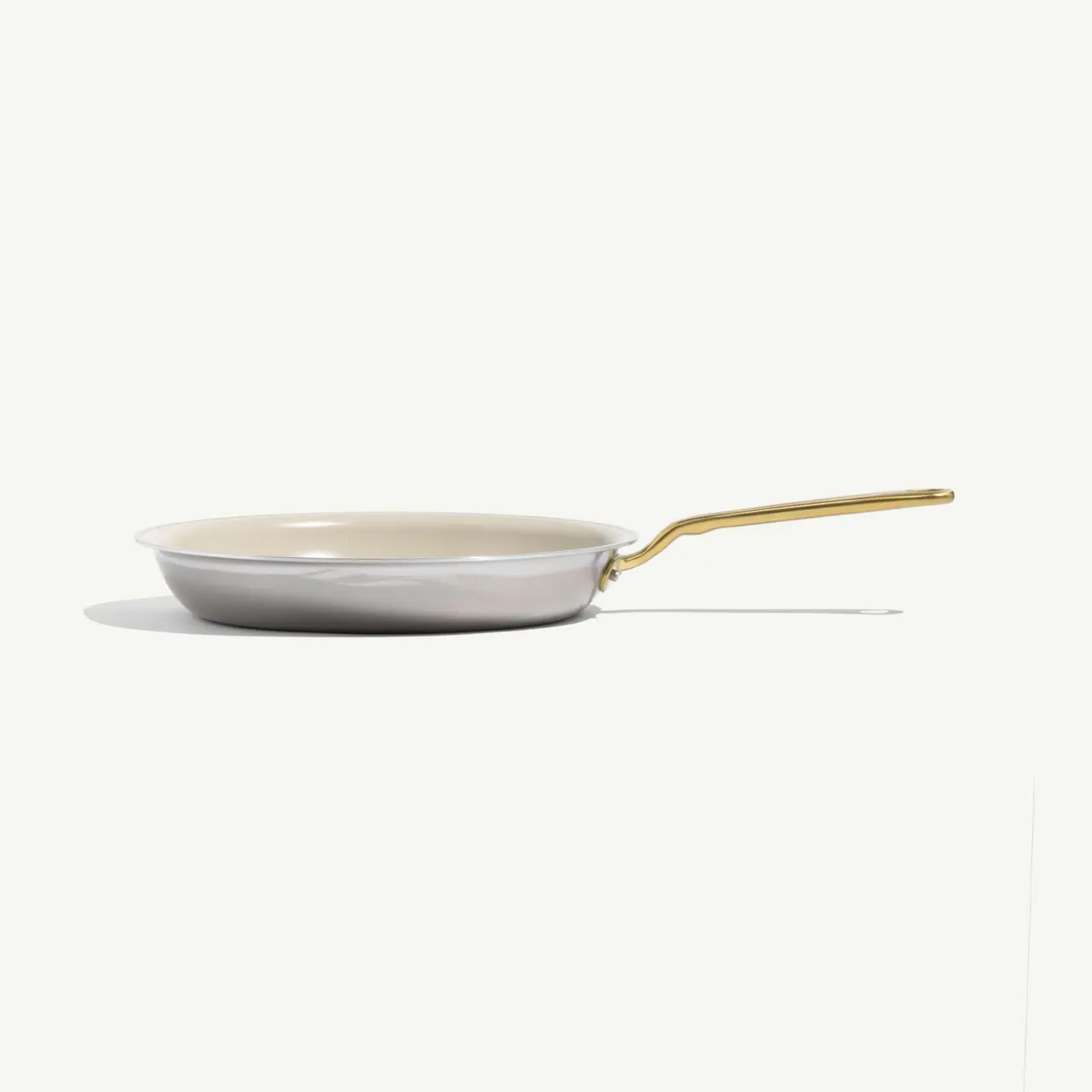 A sleek, shallow frying pan with a gold handle and a light-colored interior rests against a pale background.