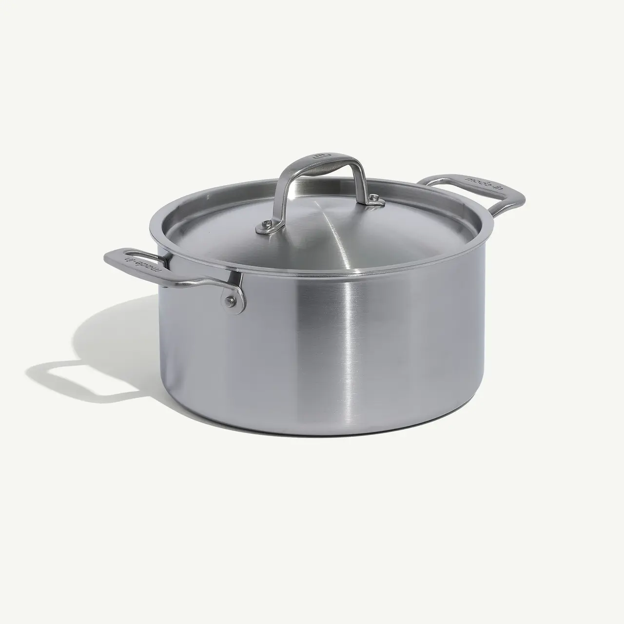 A stainless steel pot with a lid, resting on a plain surface casting a soft shadow.