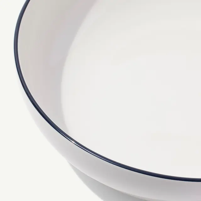 A close-up view of a white bowl with a thin blue rim on a light background.