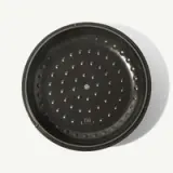 A black perforated pizza tray is captured against a light background.