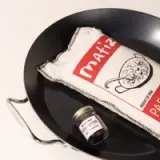 A black serving tray holds a white dish towel with red text and a fish illustration, beside a small glass jar labeled 'Sea Asparagus.'