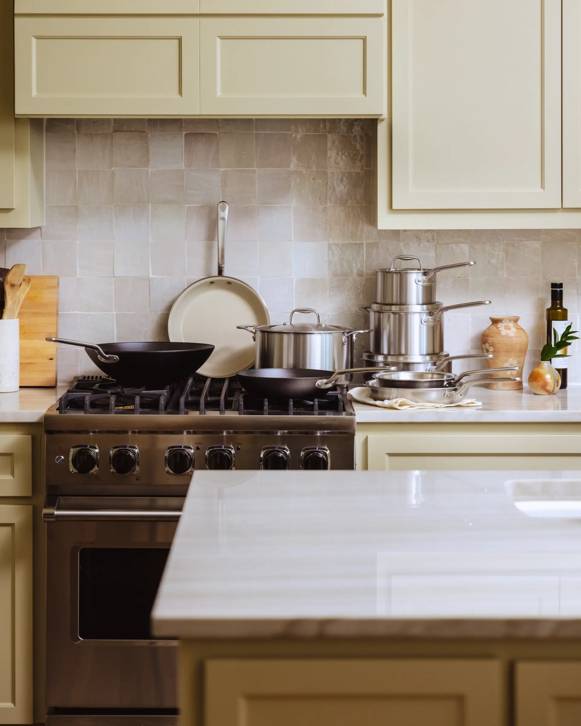 A modern kitchen features a range with cooking pots, a smooth countertop, and light-colored cabinetry.