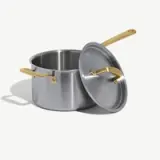 A stainless steel pot with golden handles and a lid rests partially open on a light background.