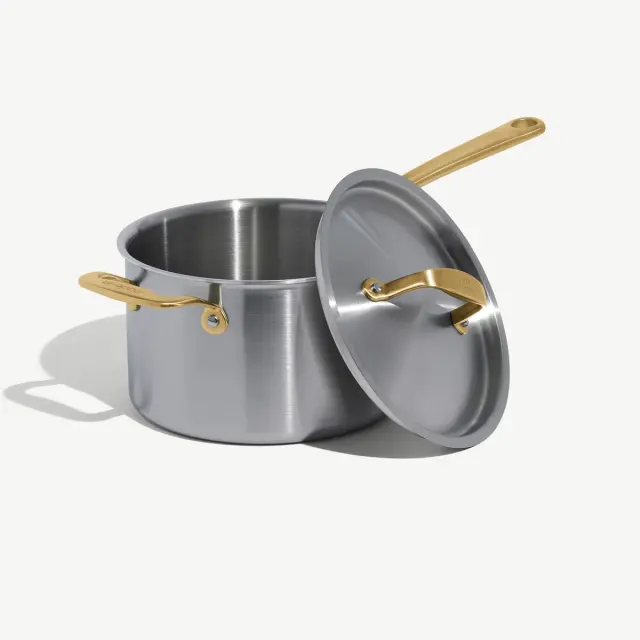 A stainless steel pot with golden handles and a lid rests partially open on a light background.