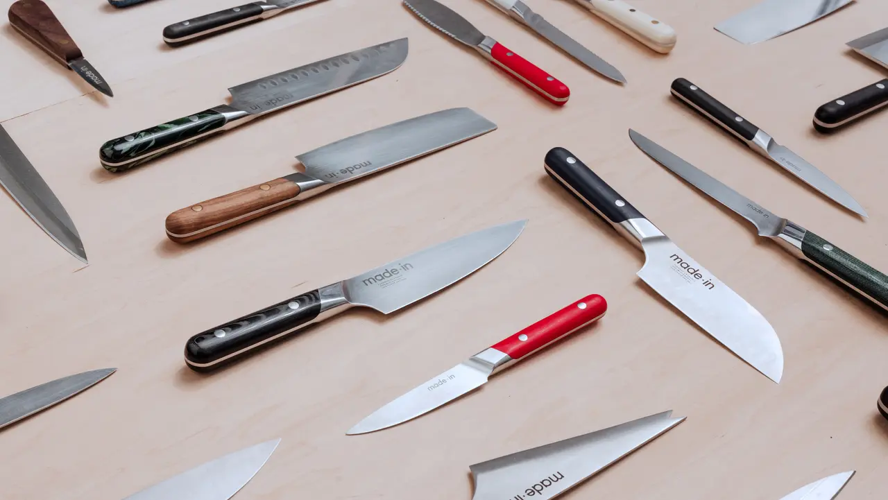 A variety of kitchen knives with different handles and blade shapes are laid out on a wooden surface.