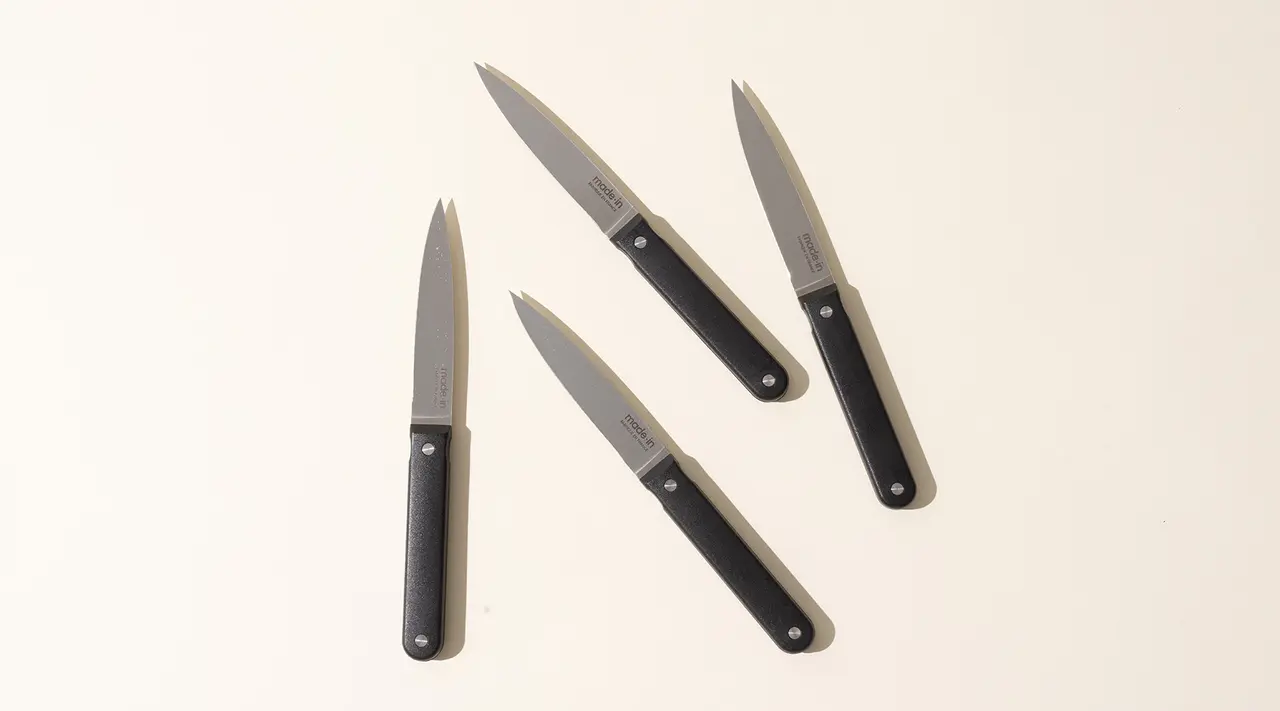 Four kitchen knives with black handles are arranged in a fan-like pattern on a light background.