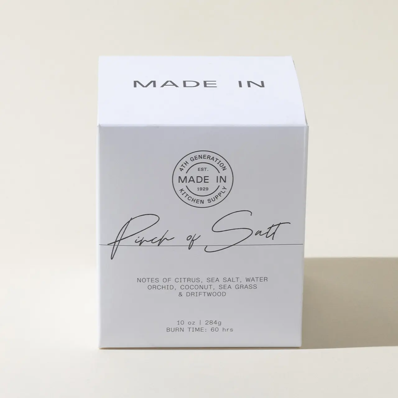 A neatly packaged 'Pinch of Salt' scented candle with a description of fragrances including citrus, sea salt, and driftwood on a plain background.