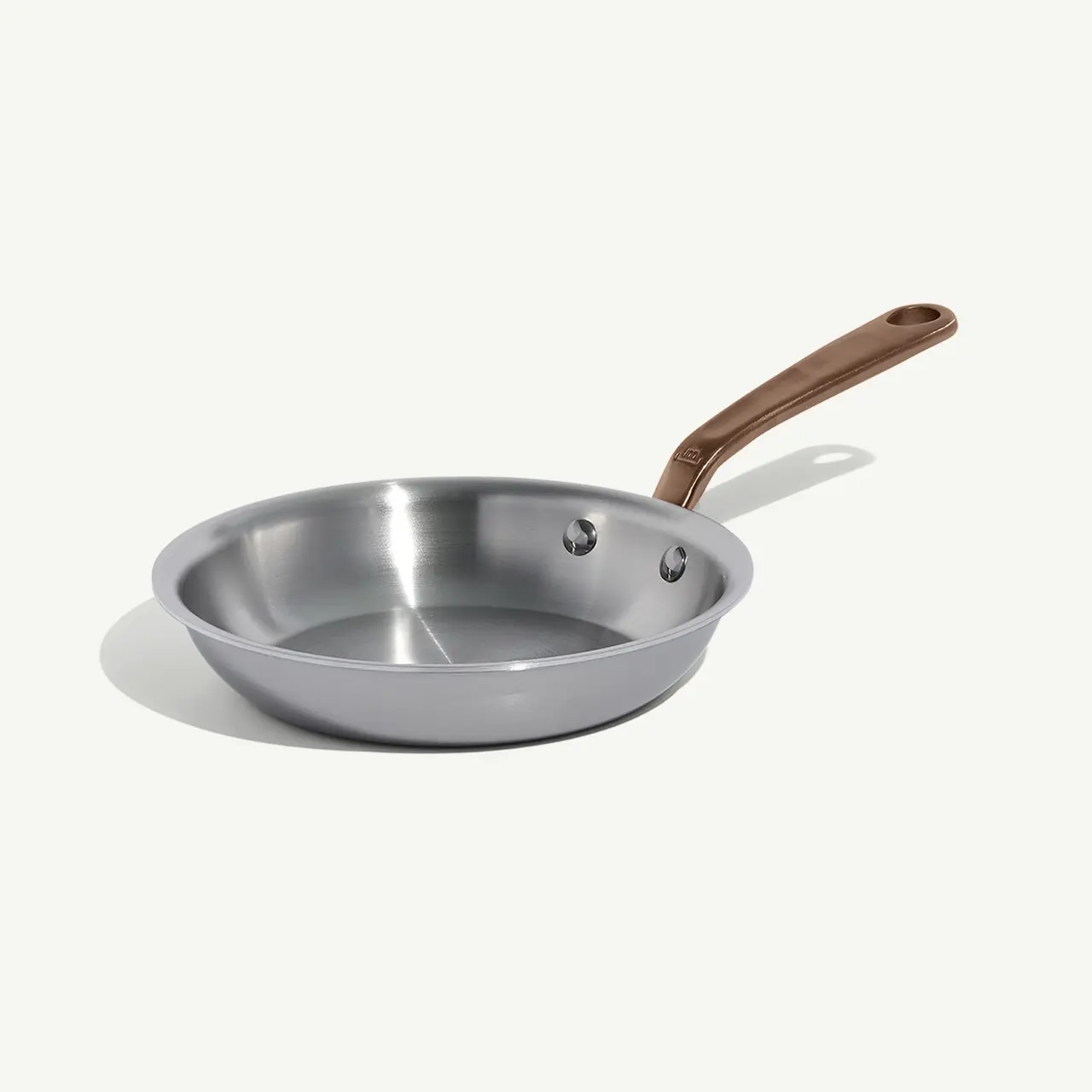 A stainless steel frying pan with a brown handle sits on a light background.