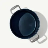 A non-stick frying pan is shown from above, casting a shadow on a light surface, with visible handles and brand markings.