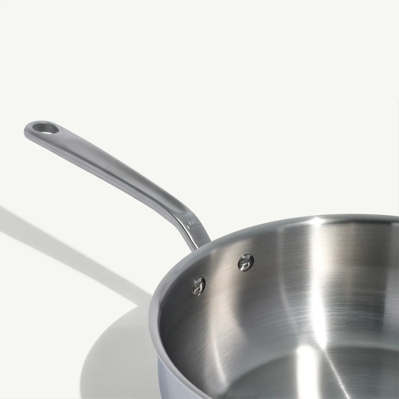 A stainless steel saucepan with a long handle casts a shadow on a light background.