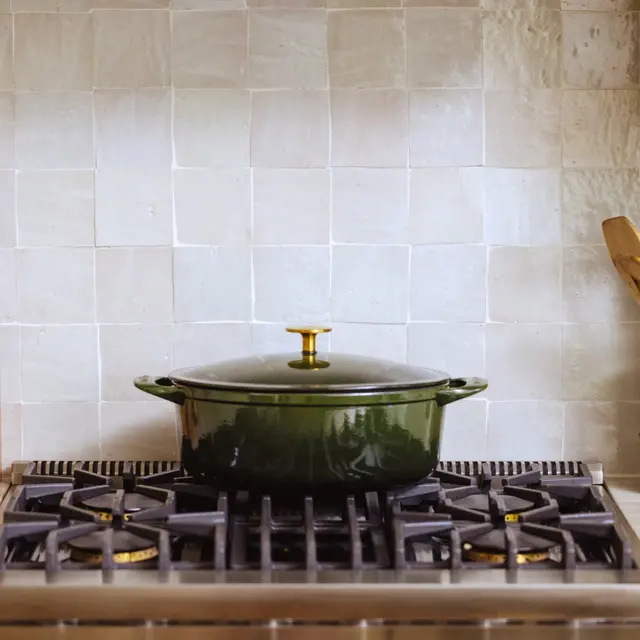 A green, lidded cooking pot sits on a modern gas stove against a backdrop of light-colored tiled walls.