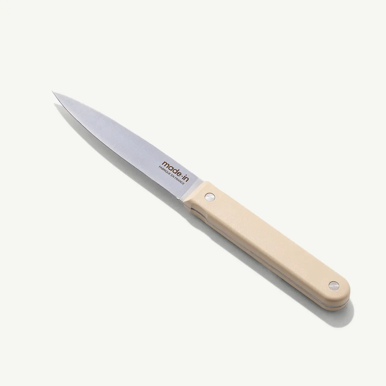 A stainless steel paring knife with a beige handle lies on a white background.