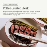 A plate features a beautifully cooked coffee-crusted steak alongside cooked asparagus, accompanied by a knife and fork.
