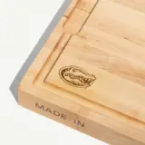 A wooden cutting board with a carved crocodile logo and the words "MADE IN" on one side.
