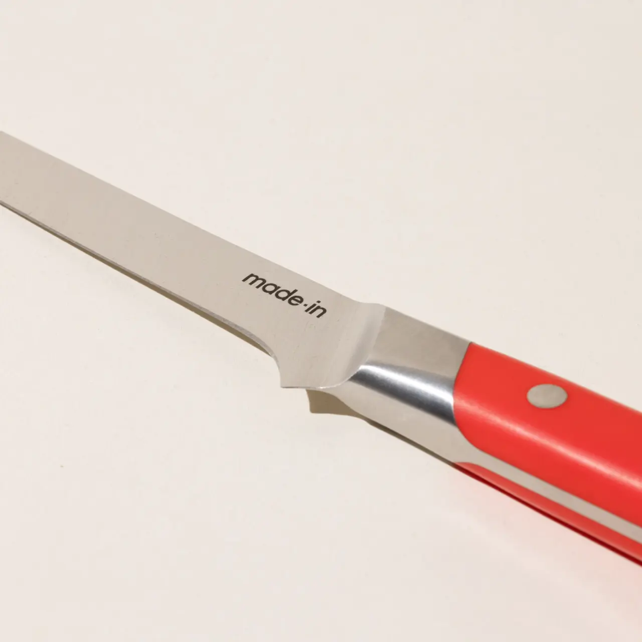 A close-up view of a kitchen knife with a red handle and "made in" engraved on the blade.