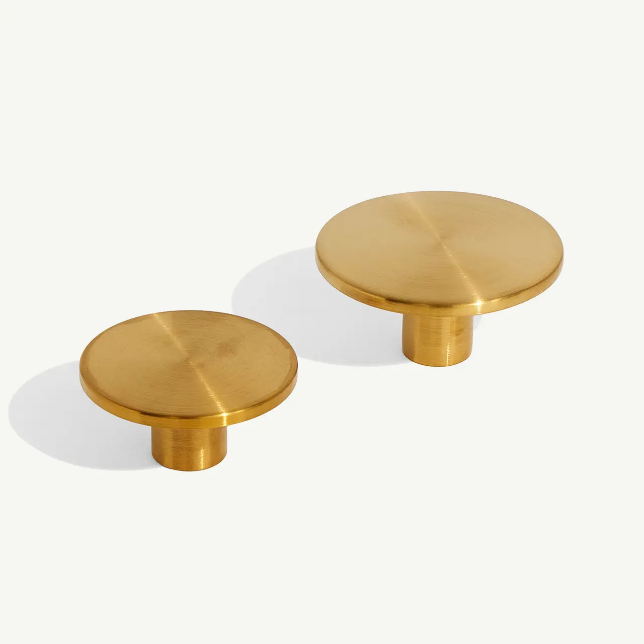 Two golden cabinet knobs are placed on a light grey surface, casting a soft shadow to one side.