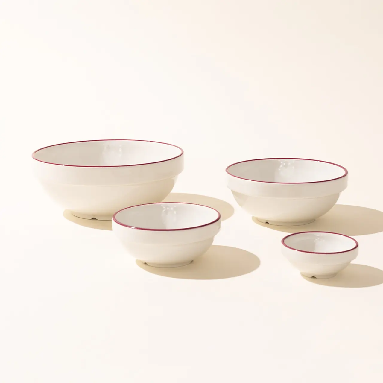 Four progressively smaller white bowls with red rims are arranged in a descending line against a beige background.