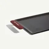 A black griddle with a red silicone handle labeled "PLATE STATE" is shown against a plain background.