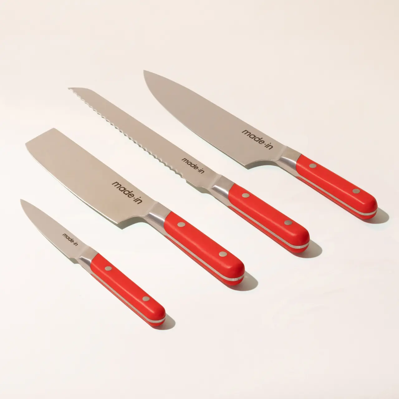Four red-handled kitchen knives with different blade shapes arranged neatly on a light background.