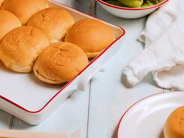 Golden-brown burger buns are arranged on a white tray with a red rim, suggesting preparation for a meal.