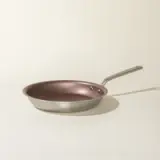 A single stainless steel frying pan with a copper-colored interior and a long handle is positioned against a neutral background.