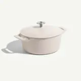 A round, pale-colored enameled cast iron pot with a lid and metallic knob sits on a light background.