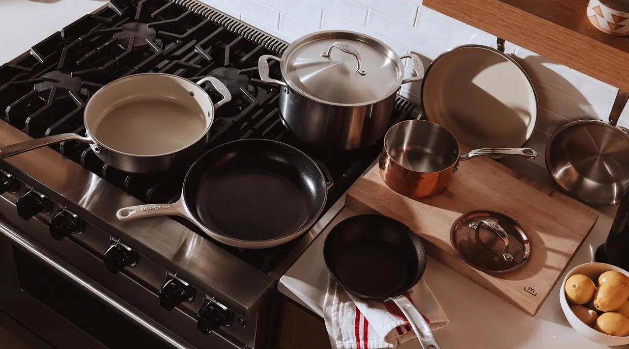 A variety of cooking pots and pans are arranged on a stovetop and countertop, showcasing a mix of materials and sizes.