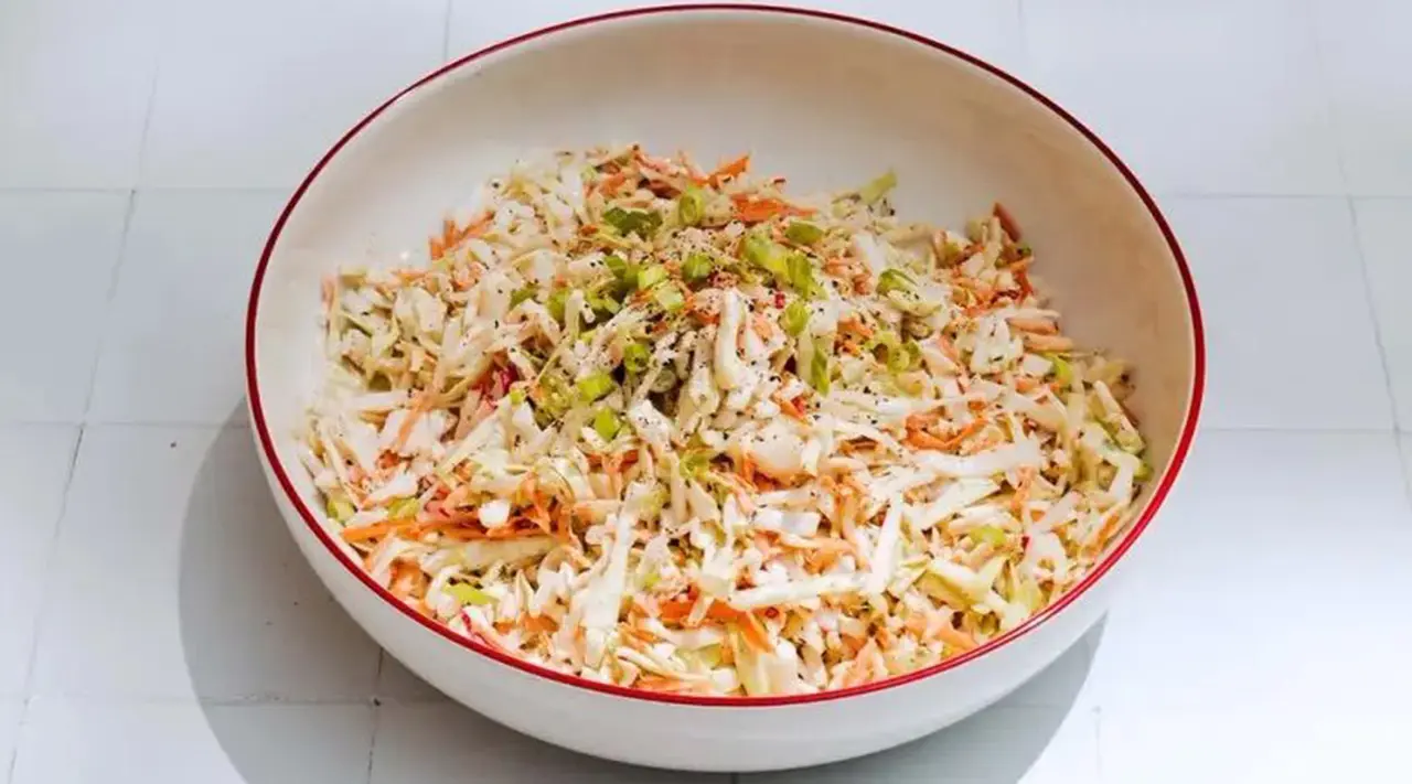 A bowl filled with coleslaw, consisting of shredded cabbage and carrots, is presented on a white surface.