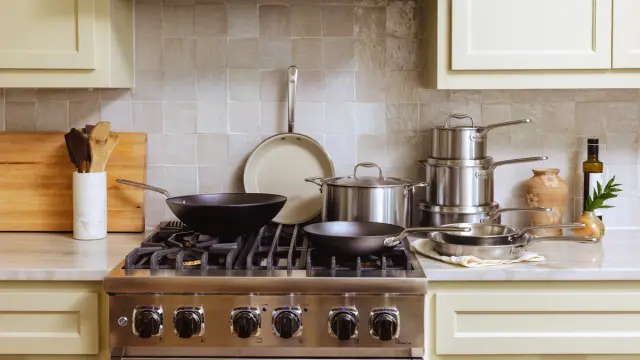 A modern kitchen countertop features a gas stove with multiple pots and pans, wooden utensils, and decorative elements.