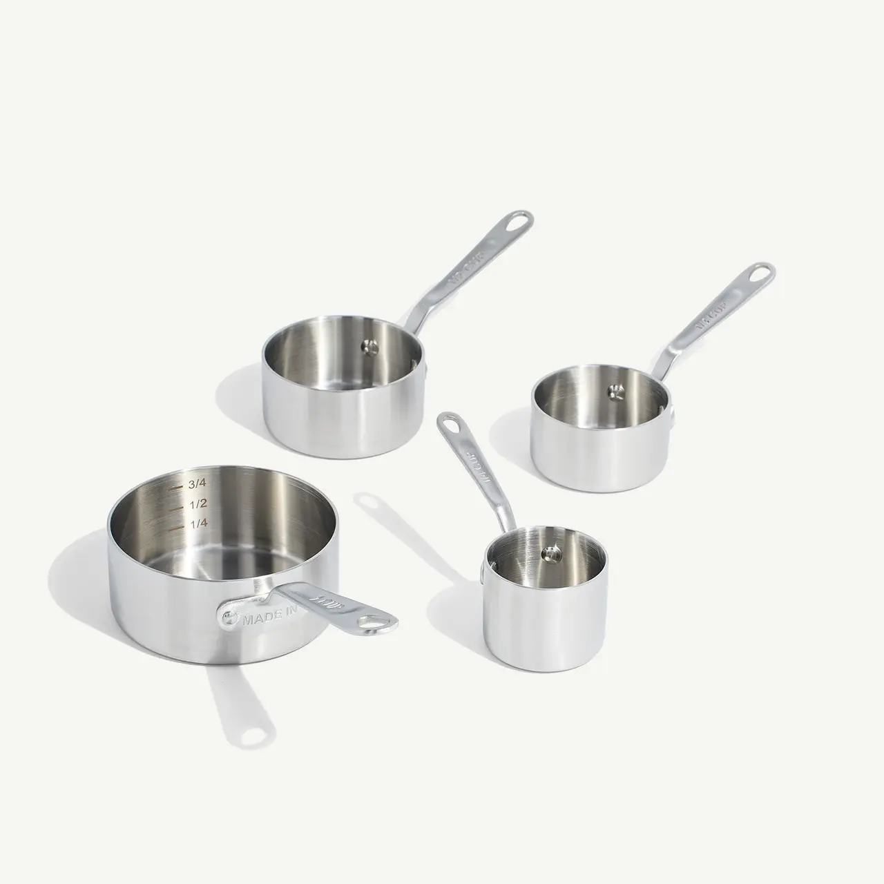 Four stainless steel measuring cups in varying sizes with long handles on a light background.