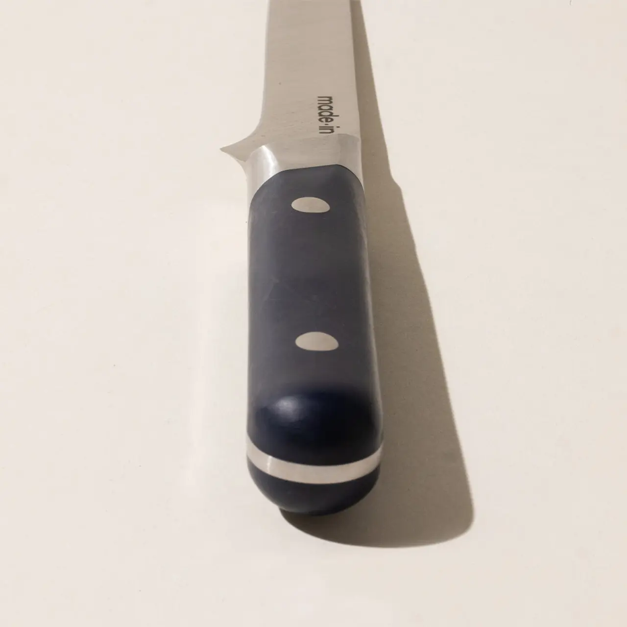A close-up of a stainless steel kitchen knife with a black handle on a light background.