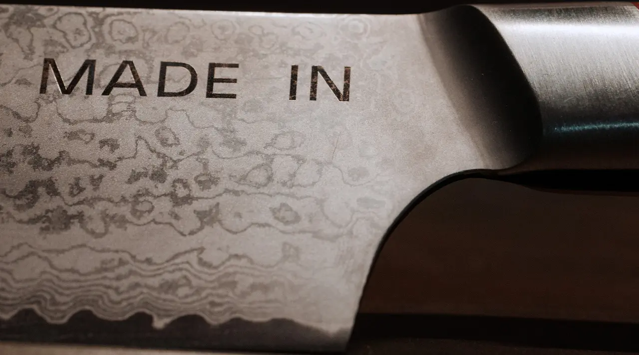 A close-up view of a knife blade with the words "MADE IN" stamped on its polished, patterned metal surface.