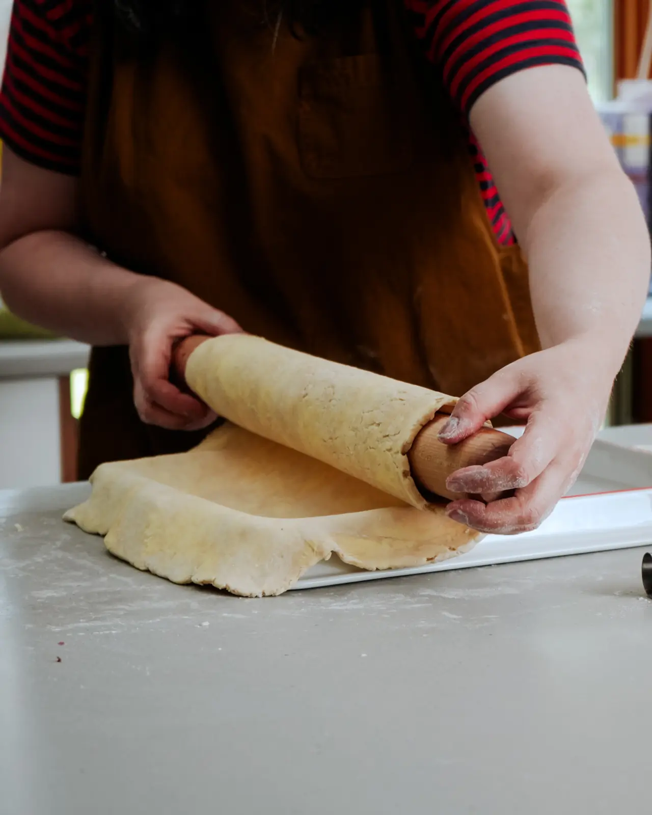 A person wearing an apron rolls out dough on a countertop using a wooden rolling pin.