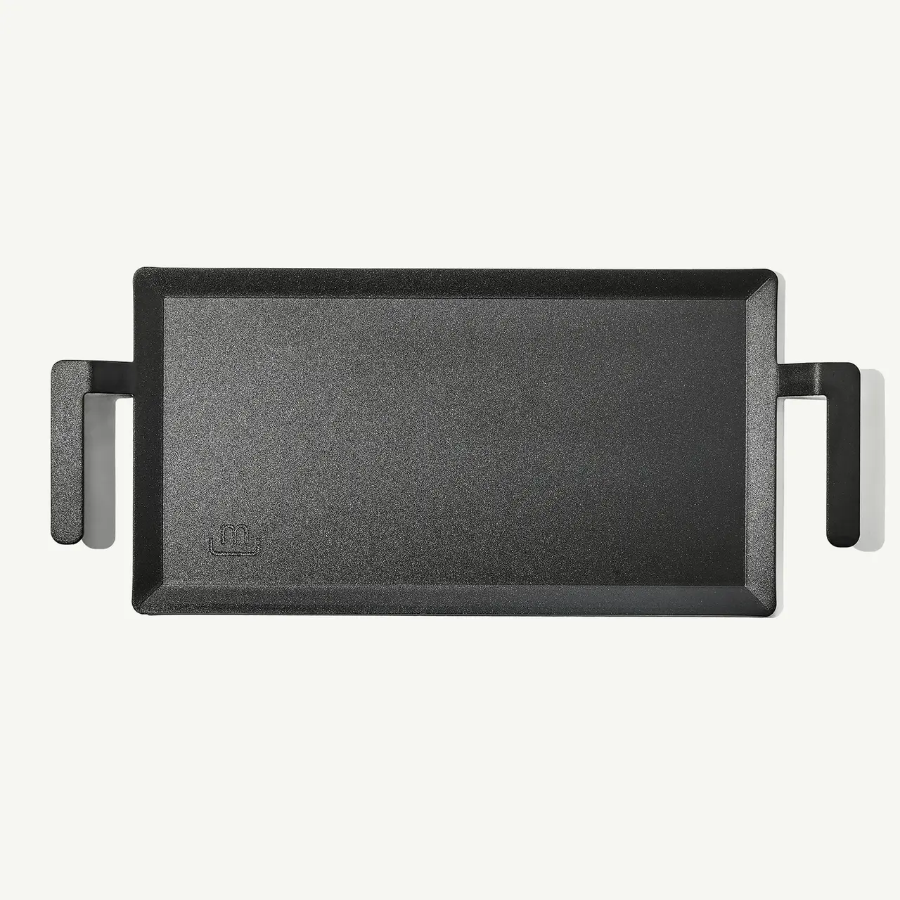 A black cast iron griddle with two handles on a light background.